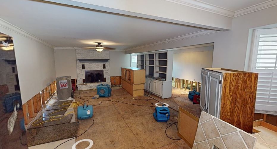 Living room water damage cleanup in progress with drying fans and equipment