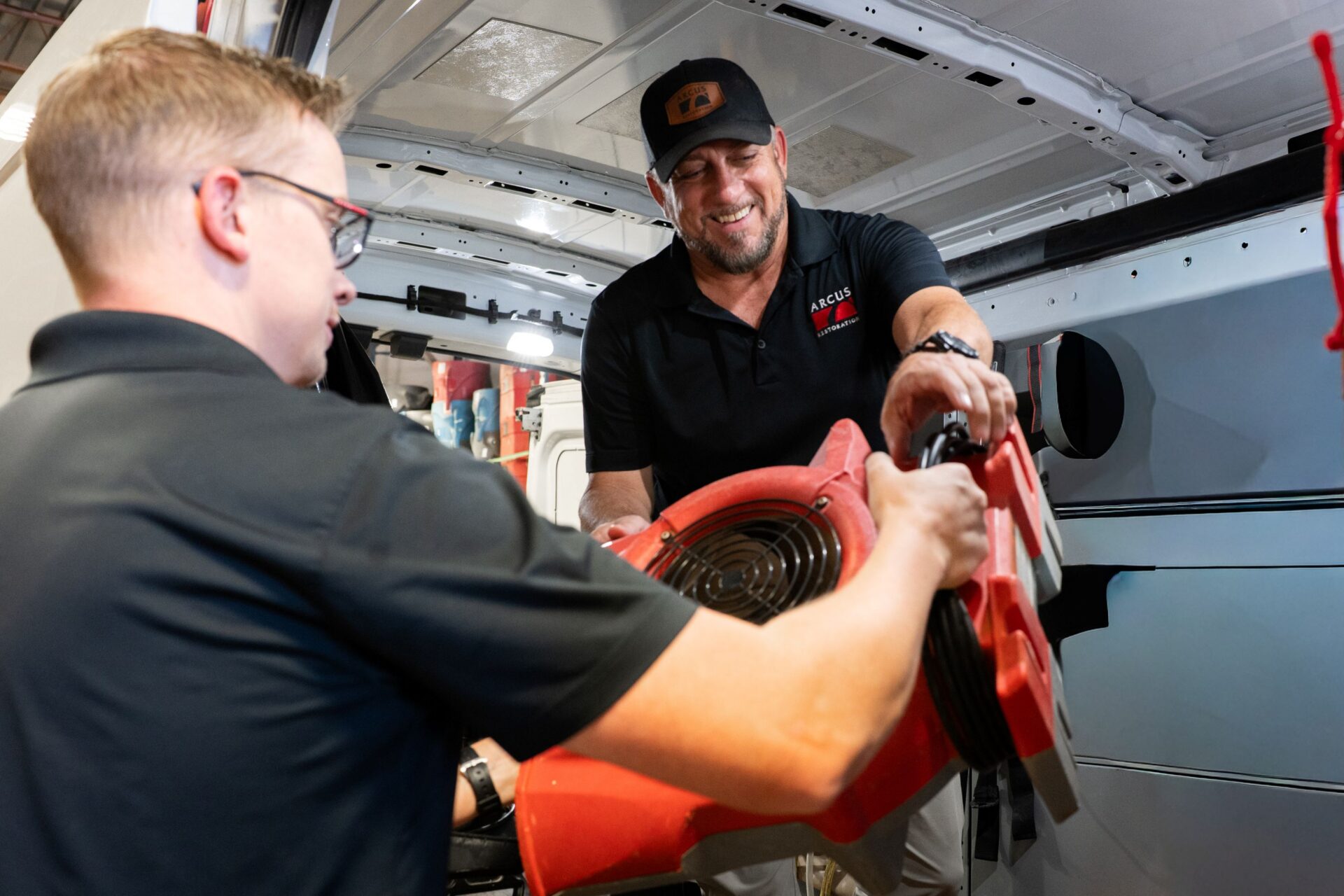 Arcus Restoration technicians preparing an air mover in a service van