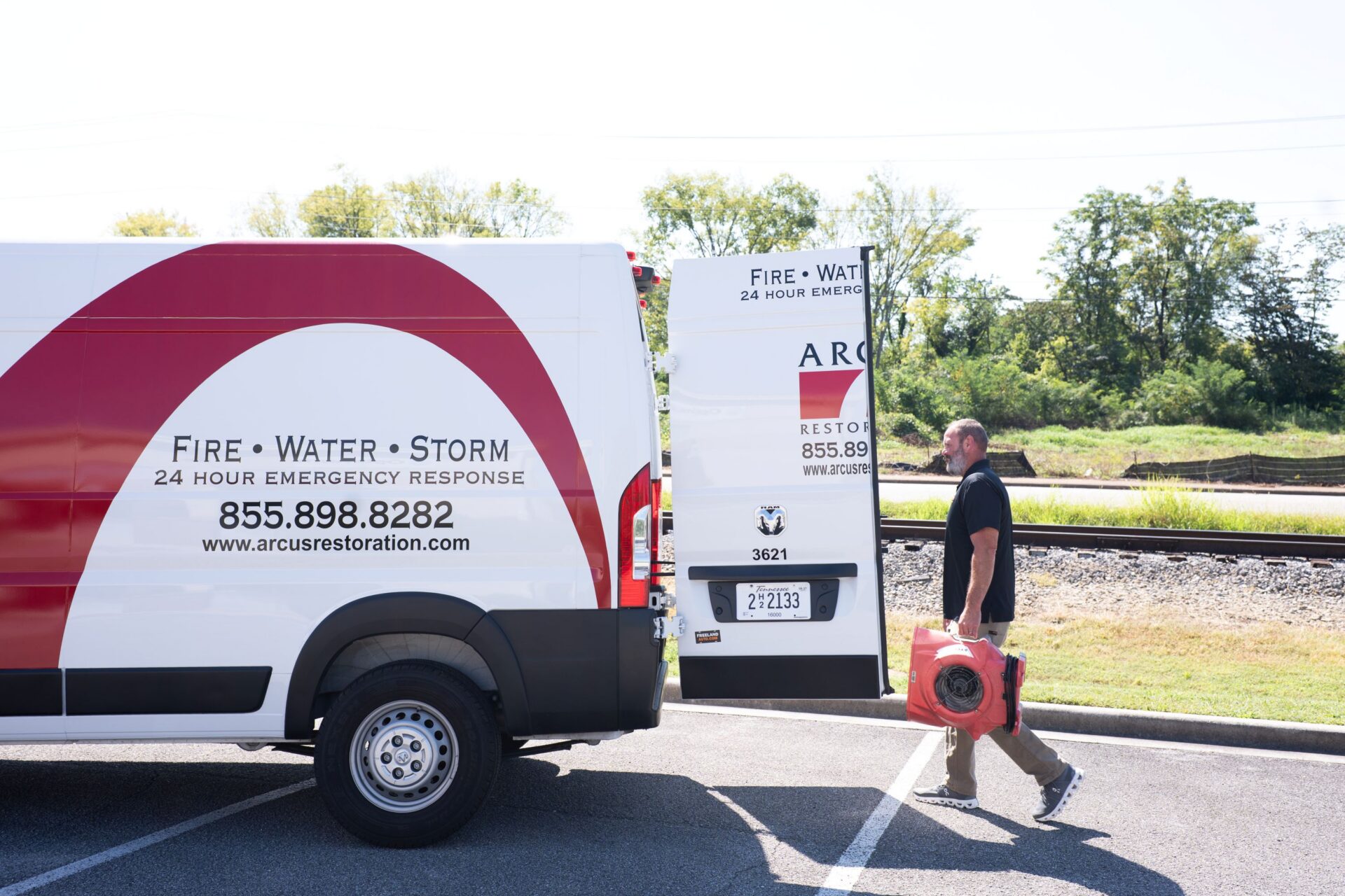 Arcus Restoration technician carrying equipment to a branded service van