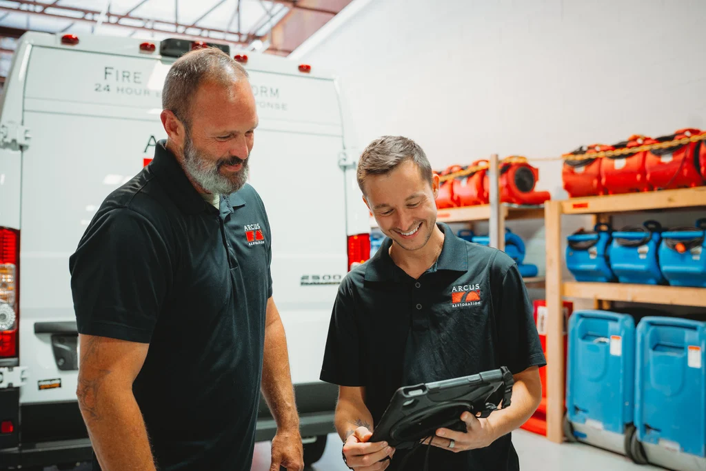 Two Arcus Restoration team members reviewing a job on a tablet in the equipment warehouse